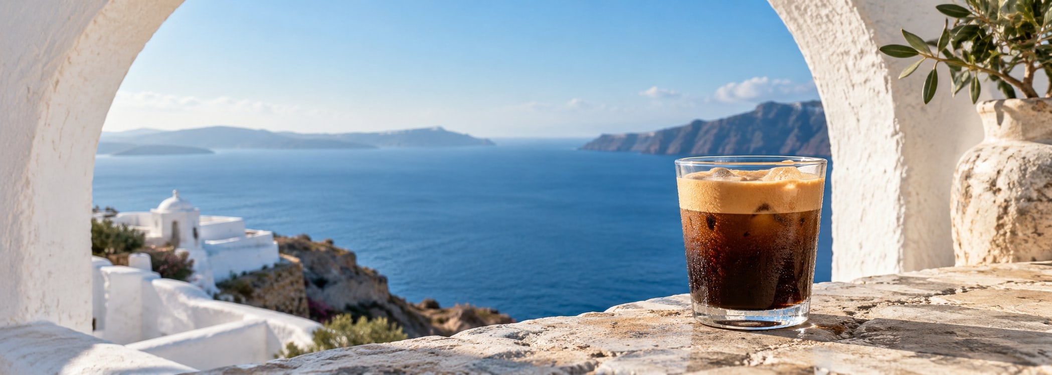 Iced Greek coffee beneath a white coastal arch
